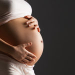 Pregnant woman caressing her belly over gray background